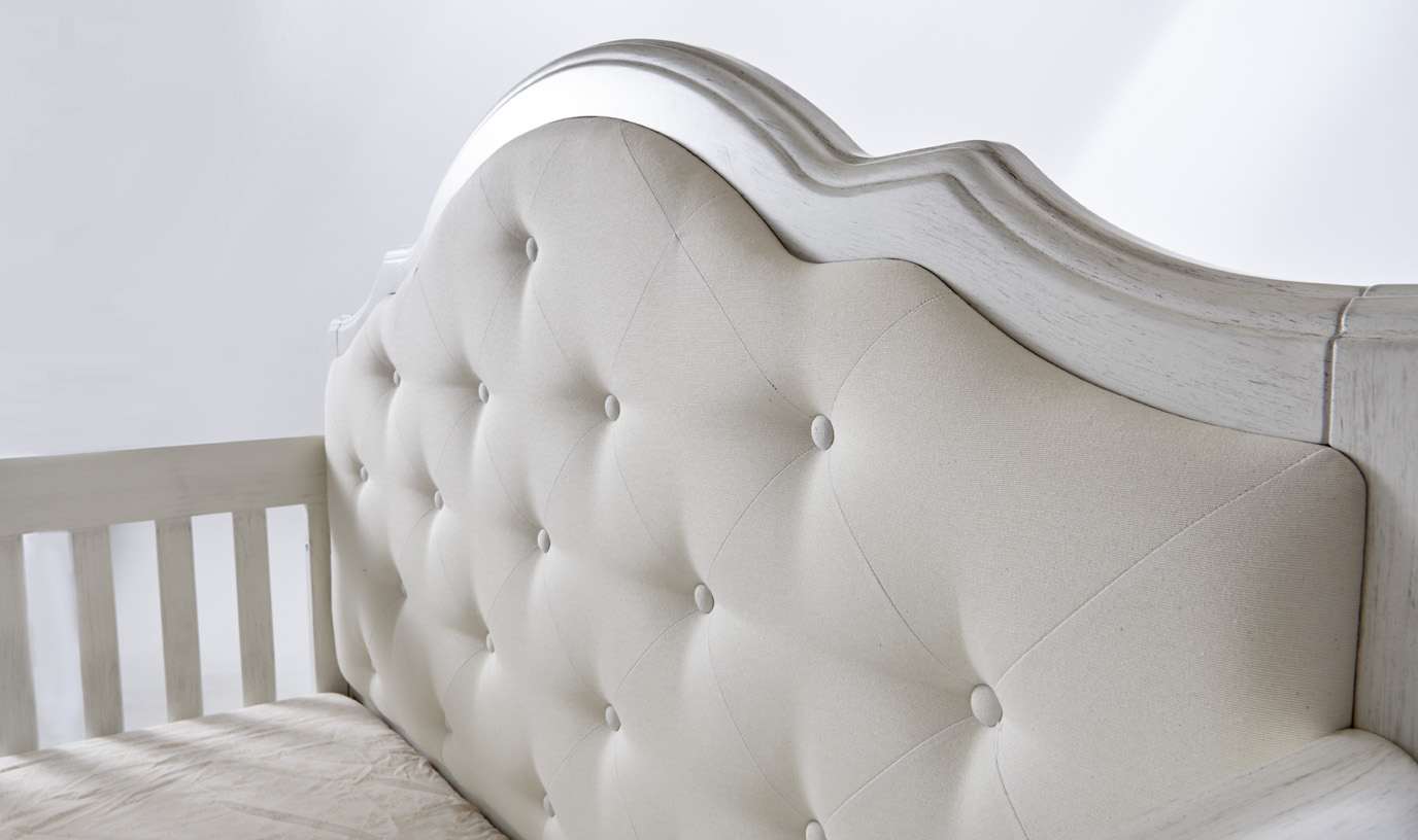 The <b>2200 Cristallo Forever Crib</b> in Vintage White with a <b>fabric upholstered panel headboard</b>. <br>The Cristallo Forever Crib is an enchanting blend of classic lines paired with sweet touches of sophisticated luxury.  The strong, clean design of this crib is highlighted by the layered moldings that frame both the front and the headpiece.  These beautifully rounded layers provide texture and a nod to the elegance of classical architecture.  Set in the headpiece of the crib is a sumptuously tufted panel. Providing a distinct sense of playful beauty, this sweetly textured cushion is designed with both style and use in mind.   